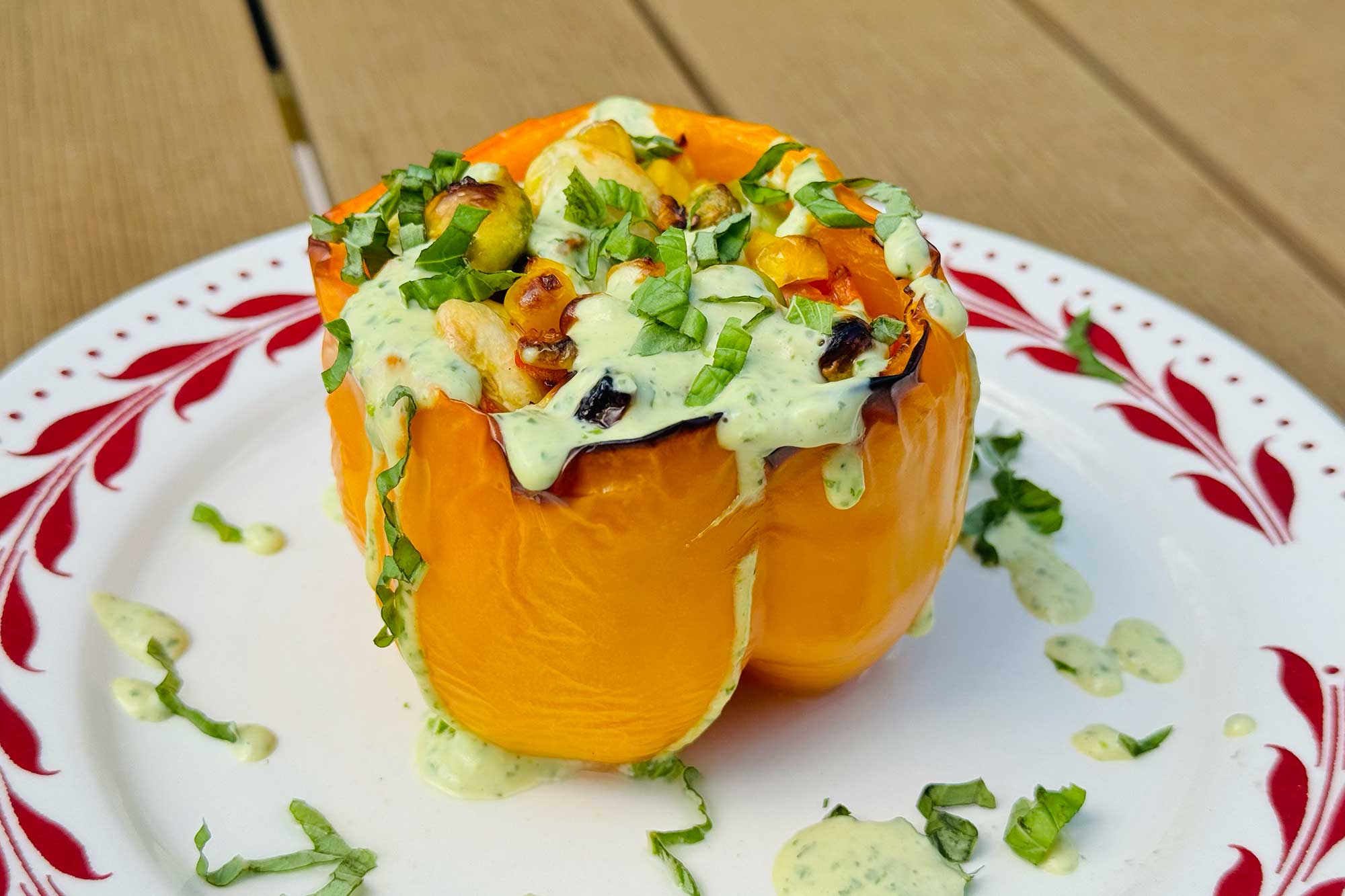 A yellow bell pepper stuffed with succotash and sitting on a white plate with a red border