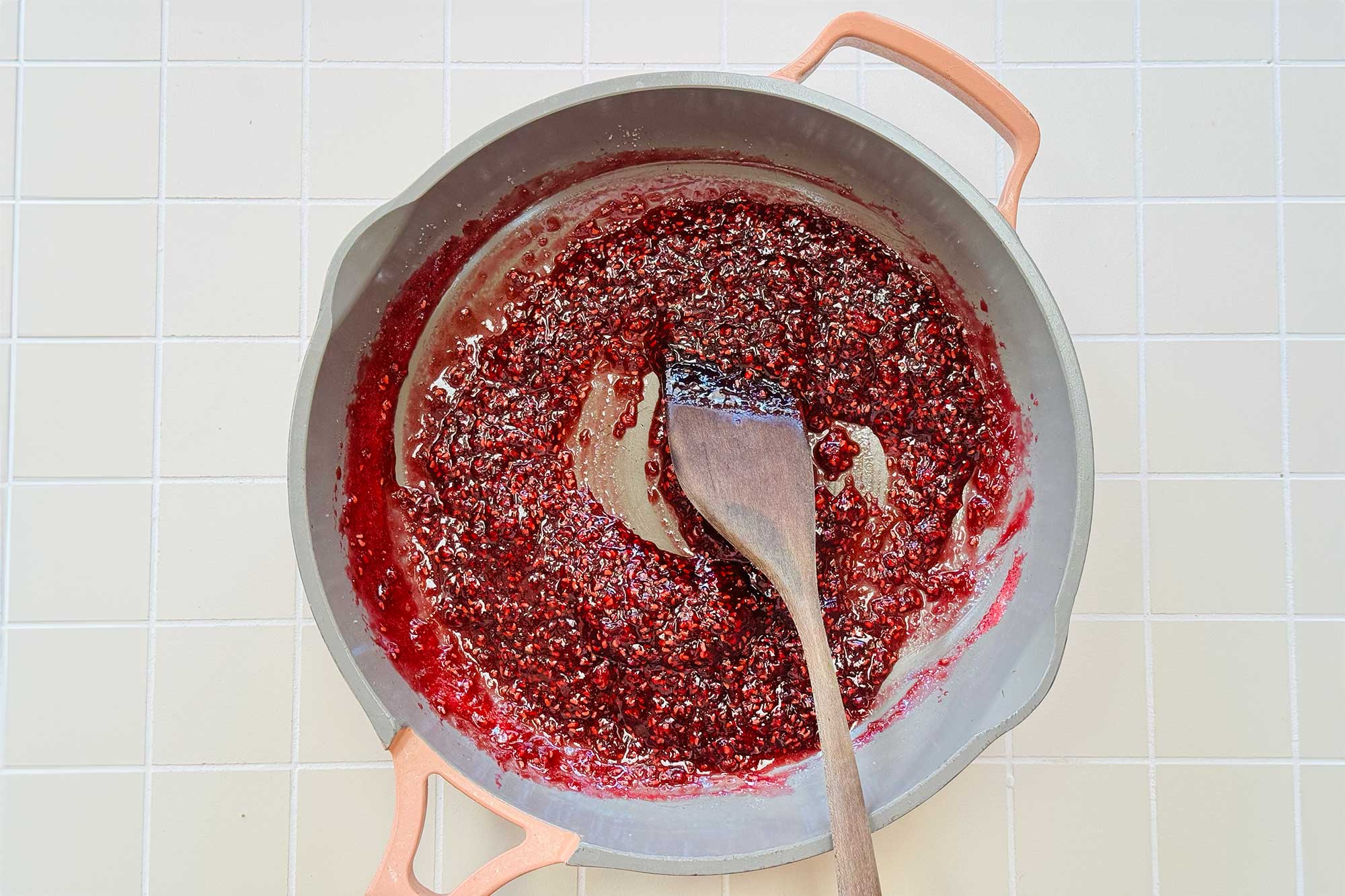 a wooden spoon stirring some skillet berry jam in a stock pot