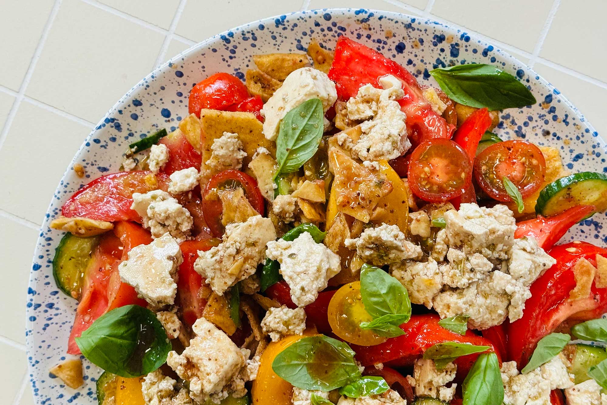 A fatoush-style salad with tomato and tofu in a speckled plate