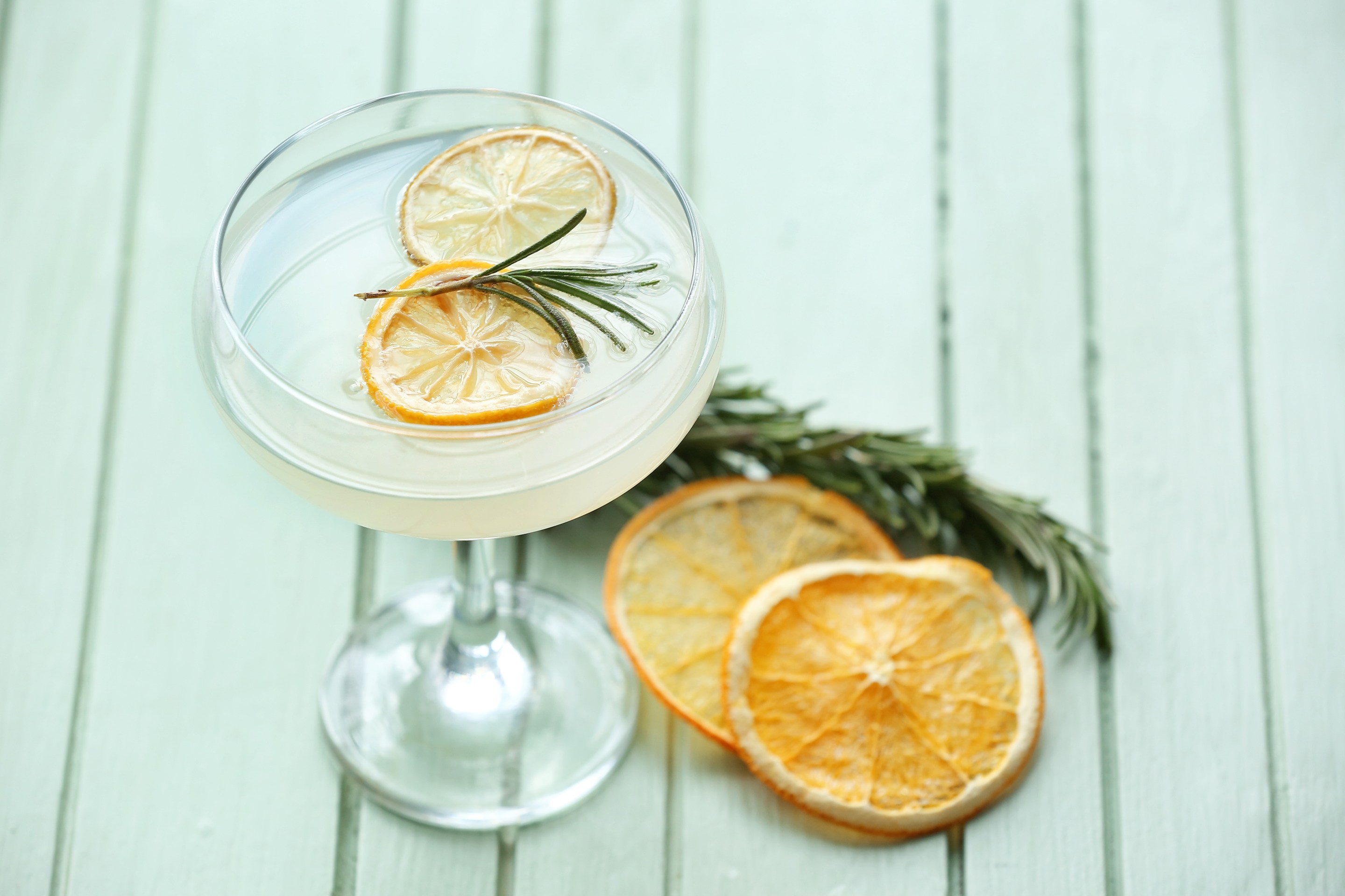 Glass of cocktail with rosemary and dried citrus fruits on color wooden background