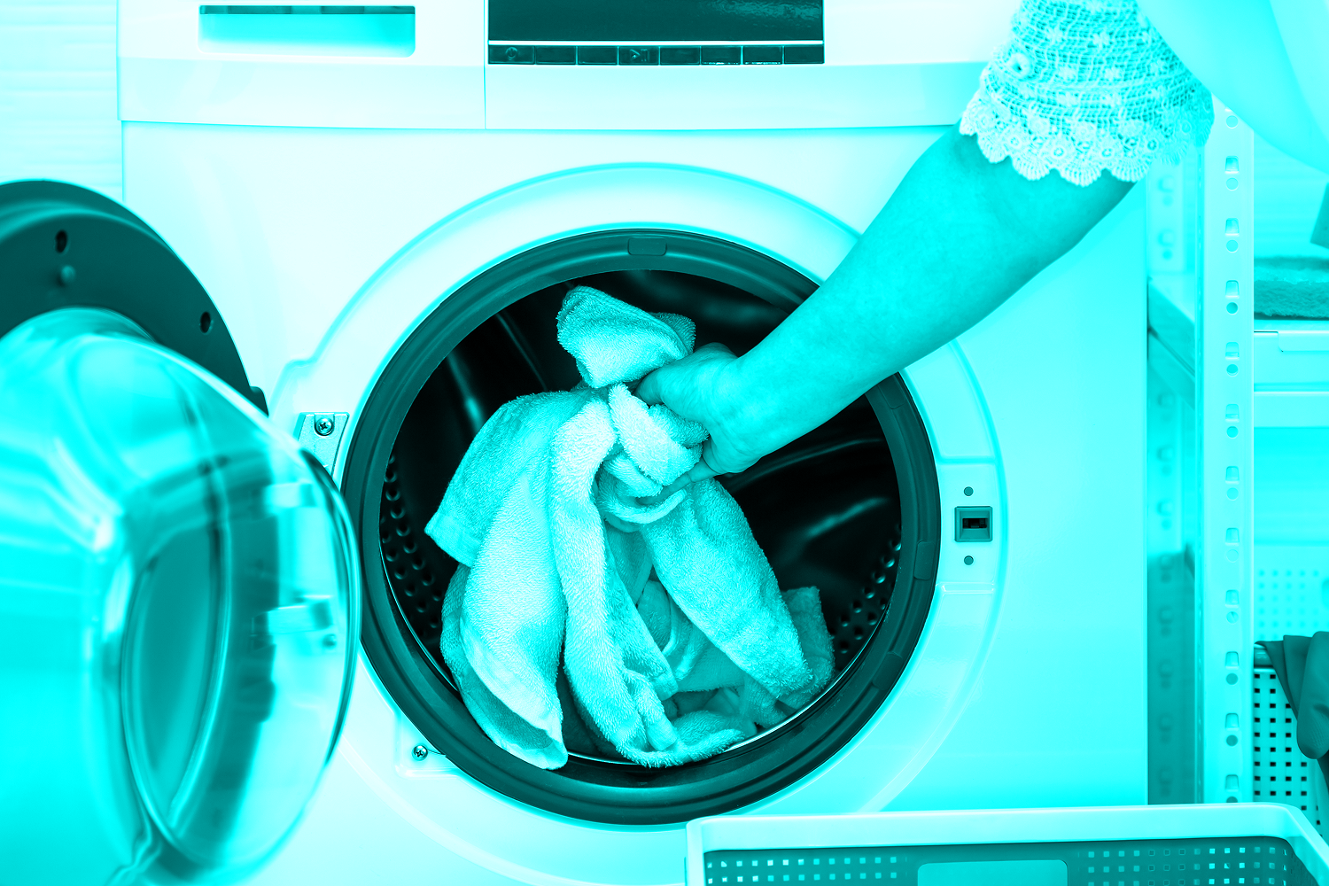 woman loading towel clothes into front load washing machine at home