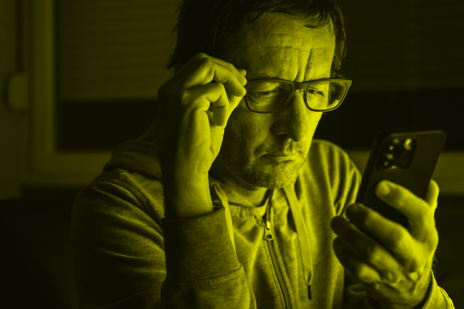 Man with glasses doomscrolling from bed