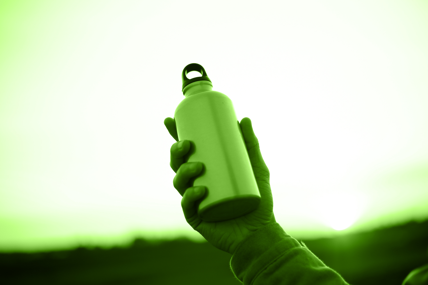 Stainless steel water bottle held in hand with sky in background